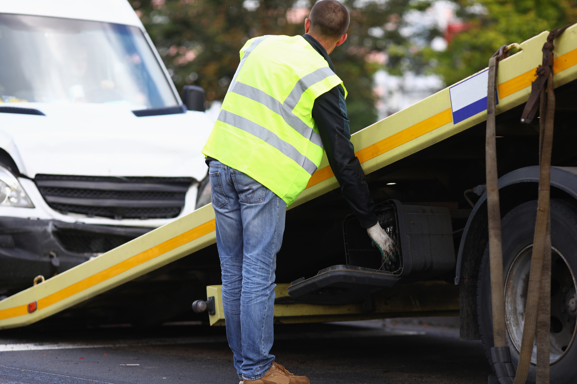 Tow truck driver loads wrecked minibus onto tow truck.